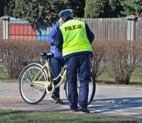 Policjant w umundurowaniu służbowym, kamizelce odblaskowej i białej czapce na głowie rozmawia z rowerzystką.