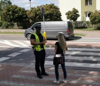 Policjant RD w umundurowaniu służbowym rozmawia z pieszą przy przejściu dla pieszych