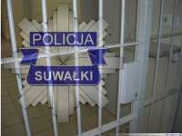 Odznaka suwalskiej Policji na tle kraty.
