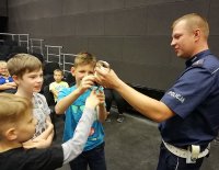 policjant w umundurowaniu służbowym pokazuje dzieciom kajdanki