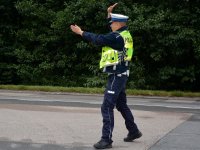 Policjant w umundurowaniu służbowym kieruje ruchem na drodze