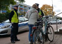 Policjanci w umundurowaniu służbowym kontrolują rowerzystkę, jadącą chodnikiem