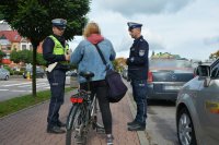 Policjanci w umundurowaniu służbowym kontrolują rowerzystkę, jadącą chodnikiem
