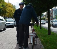 Policjanci w umundurowaniu służbowym kontrolują rowerzystę, jadącą chodnikiem