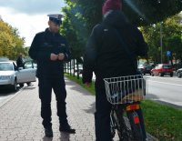 Policjanci w umundurowaniu służbowym kontrolują rowerzystę, jadącą chodnikiem