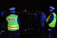 Policjanci z Wydziału Ruchu Drogowego w odblaskowych kamizelkach rozmawiają z młodymi ludźmi, ciemno, podwórko