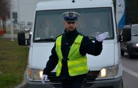 Policjant w umundurowaniu służbowym, w białej czapce i odblaskowej kamizelce kieruje ruchem drogowym