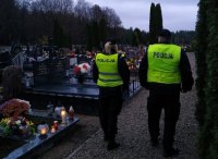 Policjanci w umundurowaniu służbowym, w odblaskowych kamizelkach patrolują cmentarz
