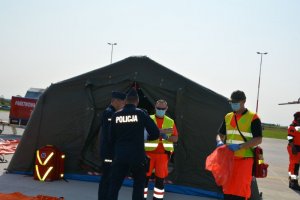 Policjanci rozmawiają z ratownikami medycznymi na tle rozbitego namiotu