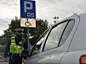 Policjant WRD w umundurowaniu służbowym kontroluje prawidłowość zaparkowania pojazdu na miejscu parkingowym dla osób niepełnosprawnych