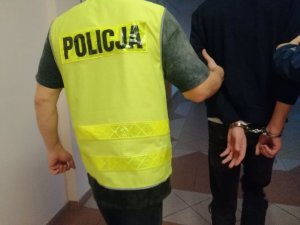 Policjant prowadzi zatrzymanego zakutego w kajdanki